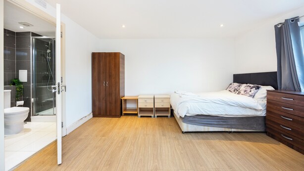 Ein Schlafzimmer mit Bett, Kleiderschrank, Nachttisch, Dusche und Toilette.