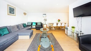 Una sala de estar moderna con un sofá modular, una mesa de centro de vidrio, un televisor de pantalla plana y un comedor con sillas y una mesa.