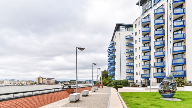 Un paseo marítimo con un moderno edificio de apartamentos, un río y una instalación de arte público.