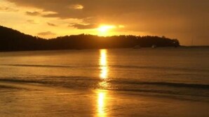Un tramonto sul mare calmo, con una terraferma boscosa all'orizzonte.
