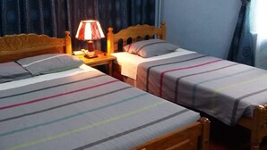 Una stanza con due letti in legno, ognuno con una coperta a righe e cuscini. Tra i letti, un comodino con una lampada.