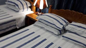 A hotel room with two beds, each with striped bedding and matching pillows. There is a wooden headboard, a nightstand with a lamp, and a curtain with a circular pattern.