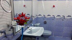 Un bagno con lavandino bianco, WC blu e uno specchio. Le pareti presentano un motivo ondulato con decorazioni di delfini.