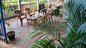 Patio esterno con tavoli e sedie di legno, circondato da un recinto in metallo e piante in vaso.