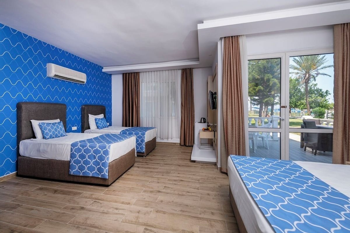 A hotel room with two beds, a large window, and a balcony with outdoor furniture.