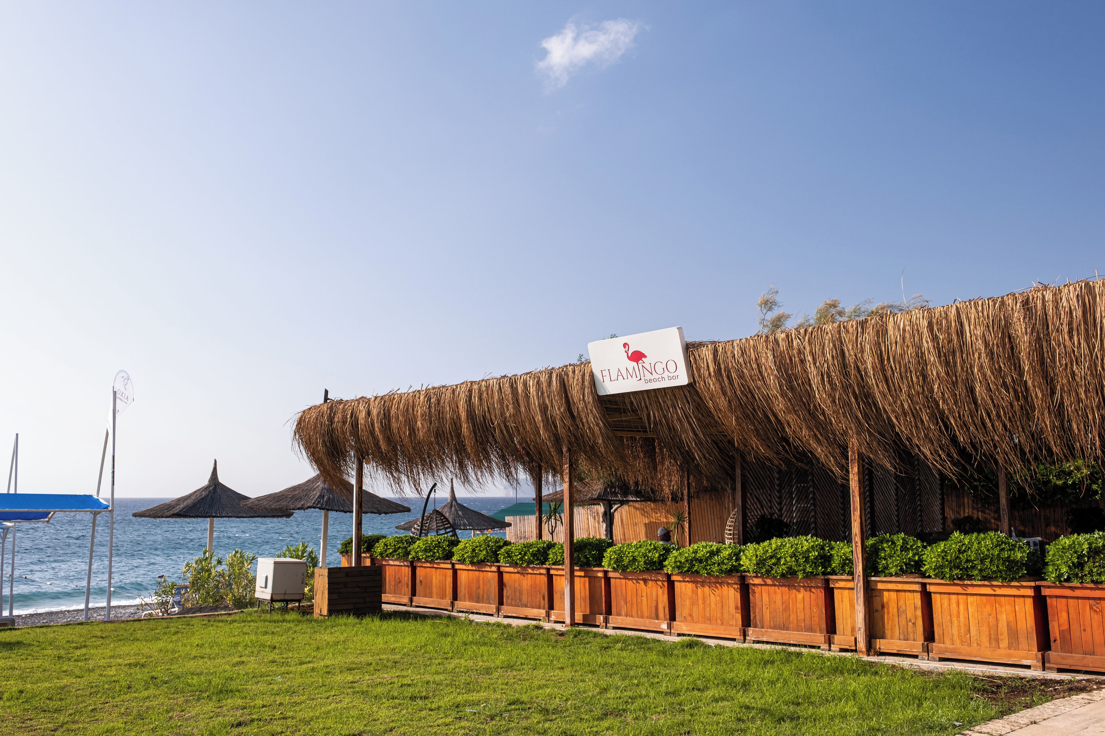 A beachside restaurant with a thatched roof and wooden deck, overlooking the sea.