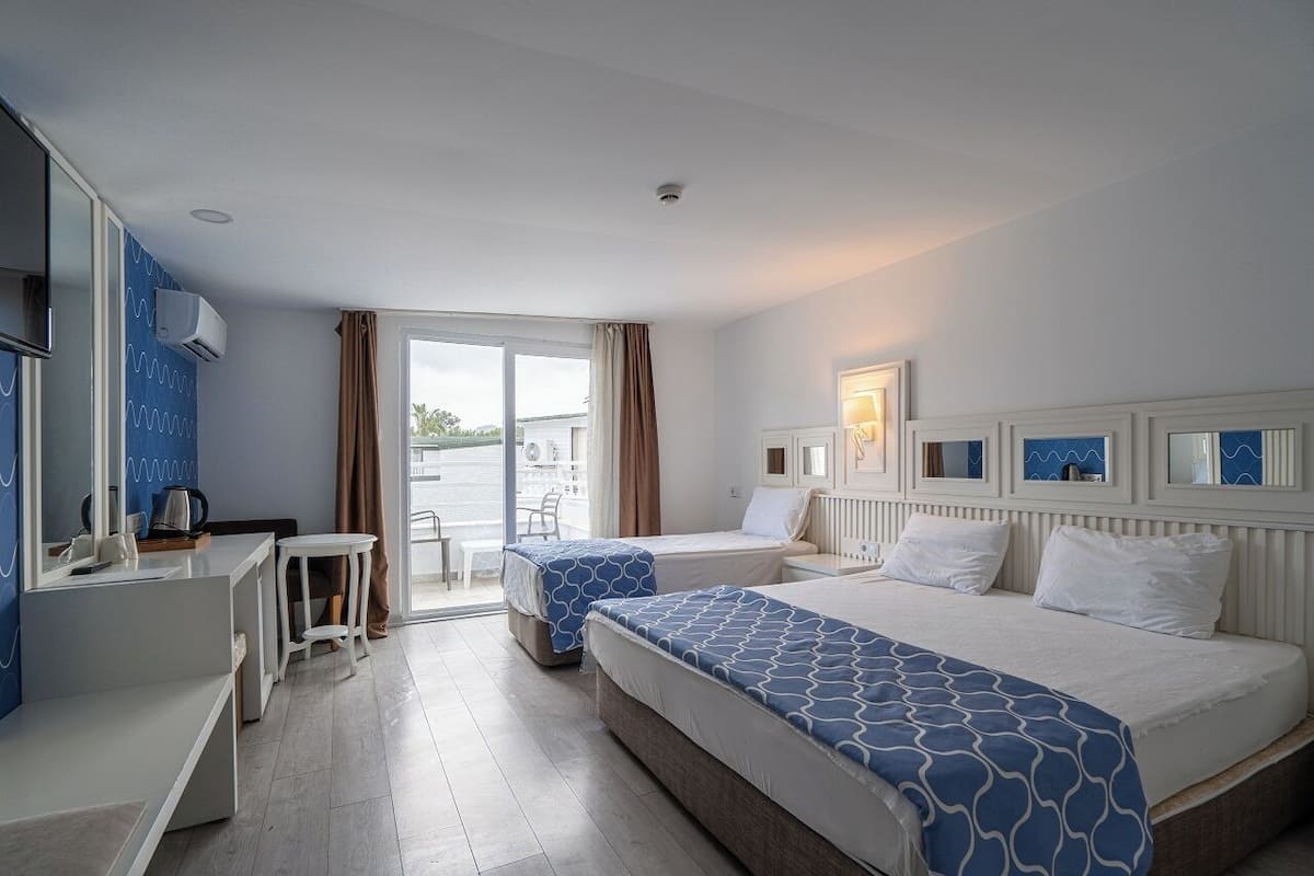 A hotel room with two beds, a desk, a chair, and a view of the sea.