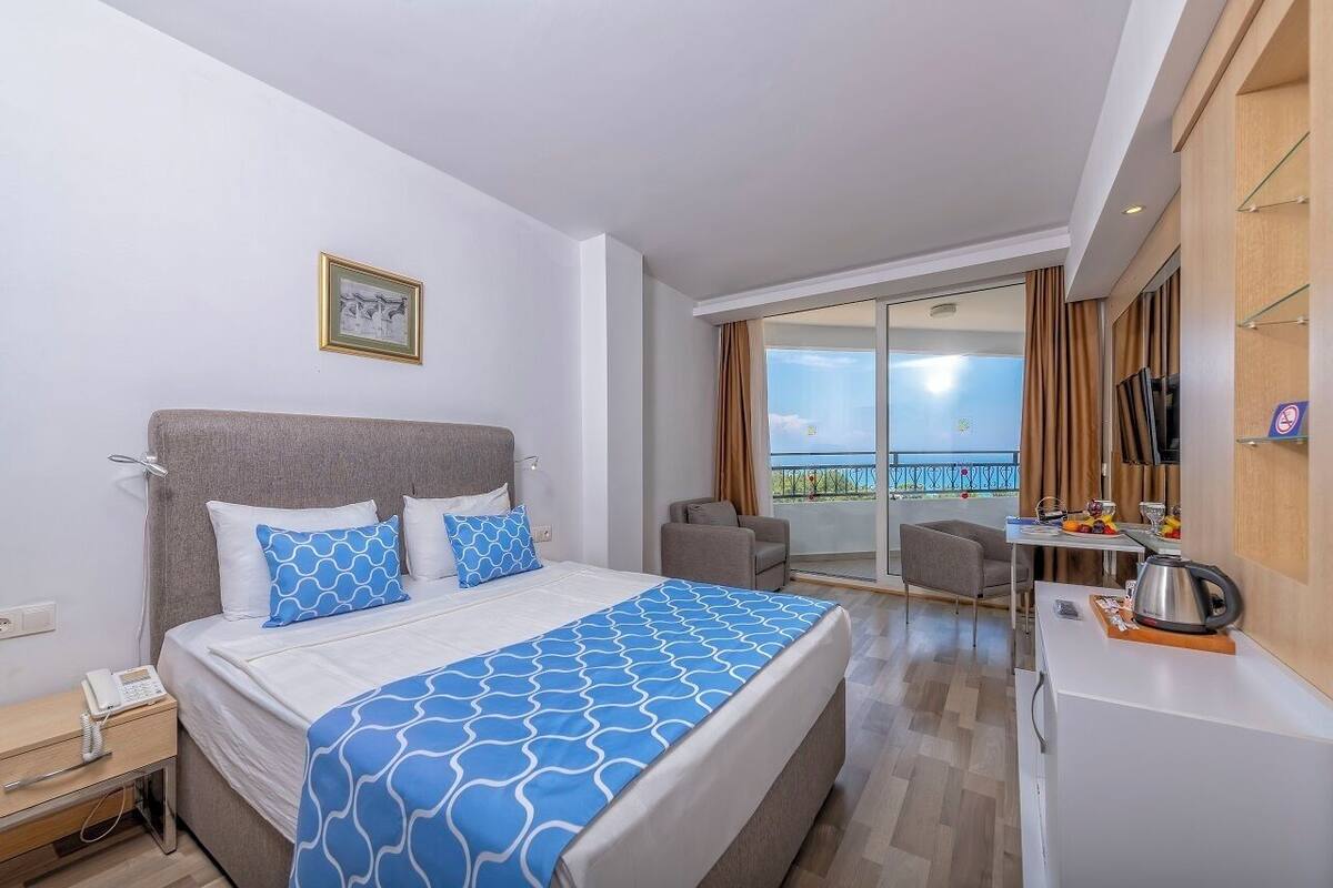 A modern hotel room with a large bed, a desk, and a balcony with a view.