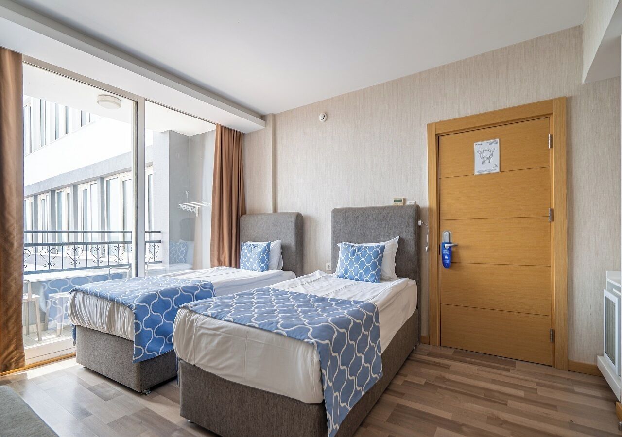 Una habitación de hotel con dos camas, una puerta de madera y un balcón con vistas a edificios.