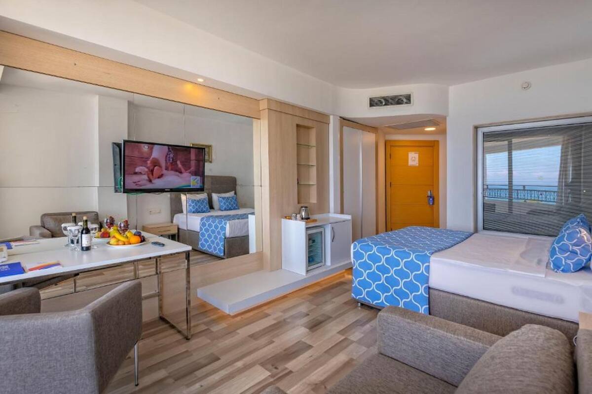 A modern hotel room with a bed, a TV, a dining area, and a balcony.