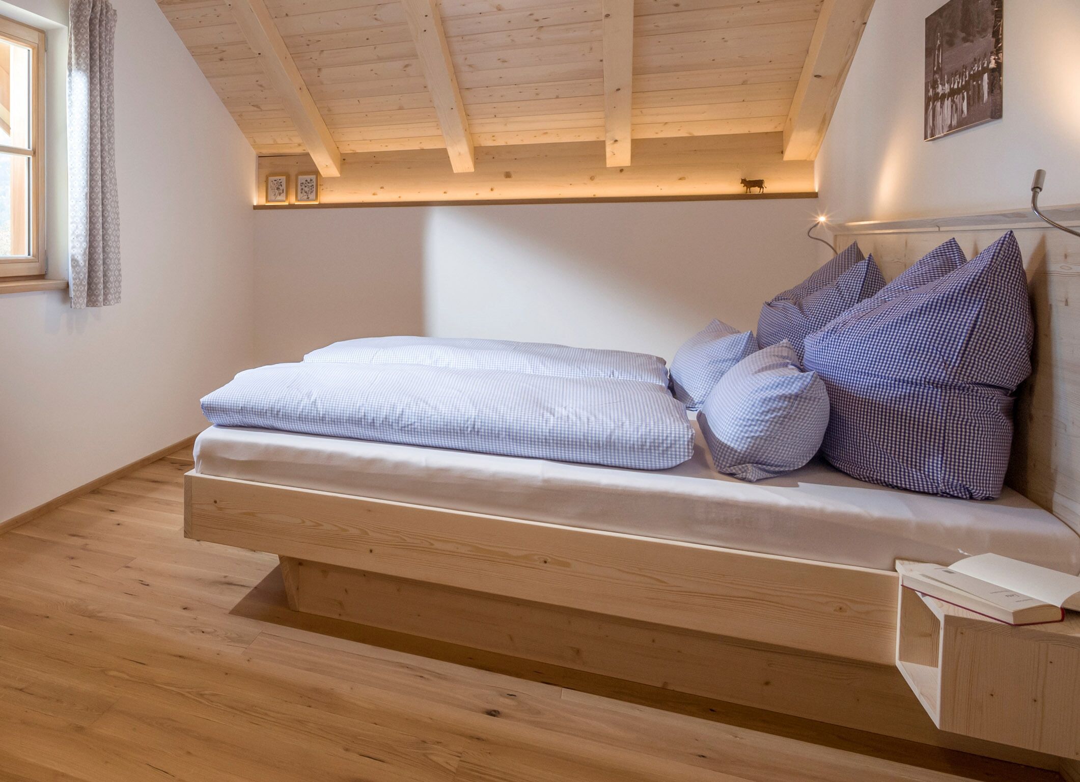 Une chambre de style loft avec un plafond en bois, un lit avec une literie bleue et blanche, et une petite table de chevet sur laquelle repose un livre.