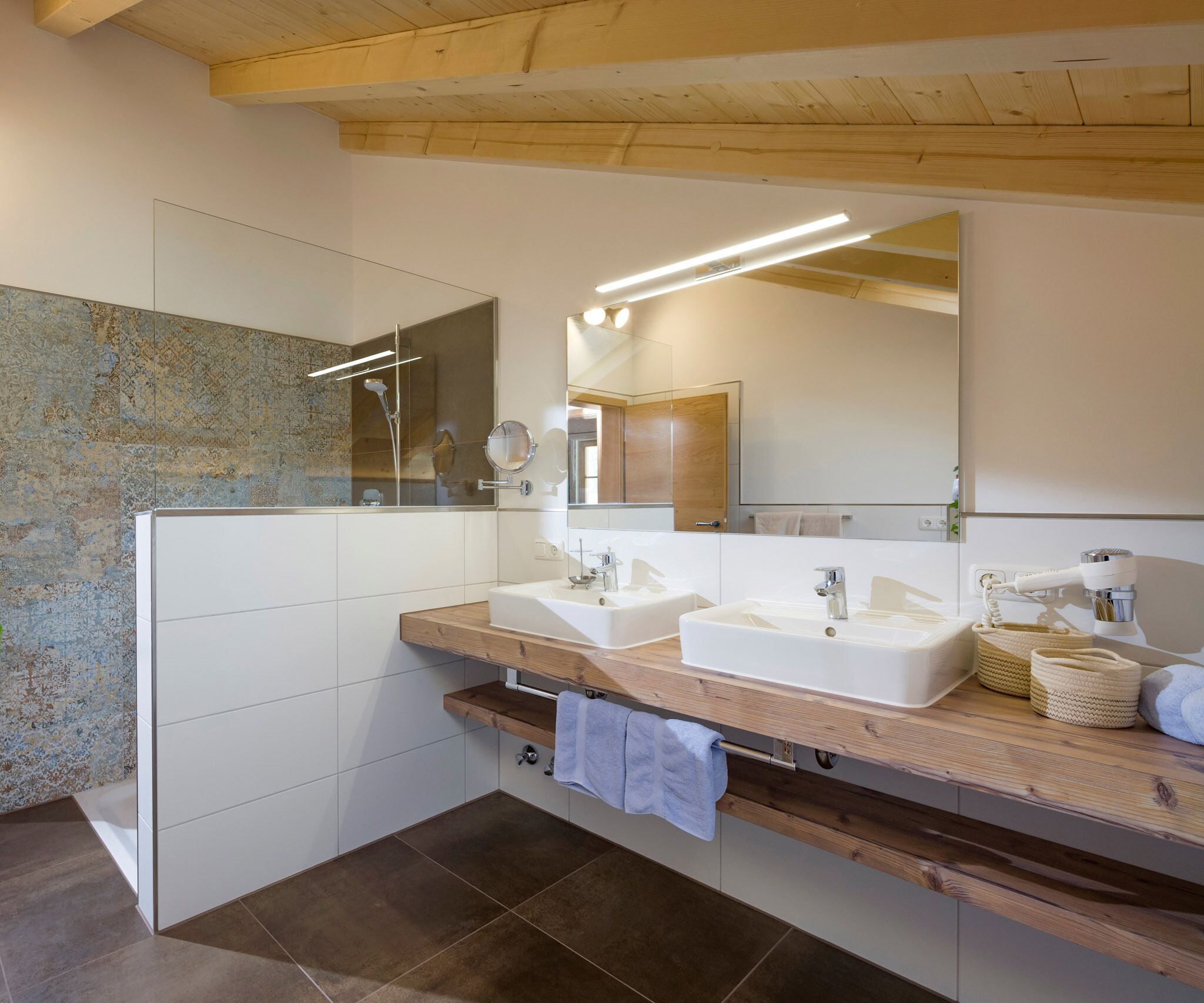 Ein modernes Badezimmer mit zwei Waschbecken, einem großen Spiegel und einer Dusche.