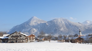 Un village enneigé, avec des bâtiments traditionnels et une église, entouré de montagnes.