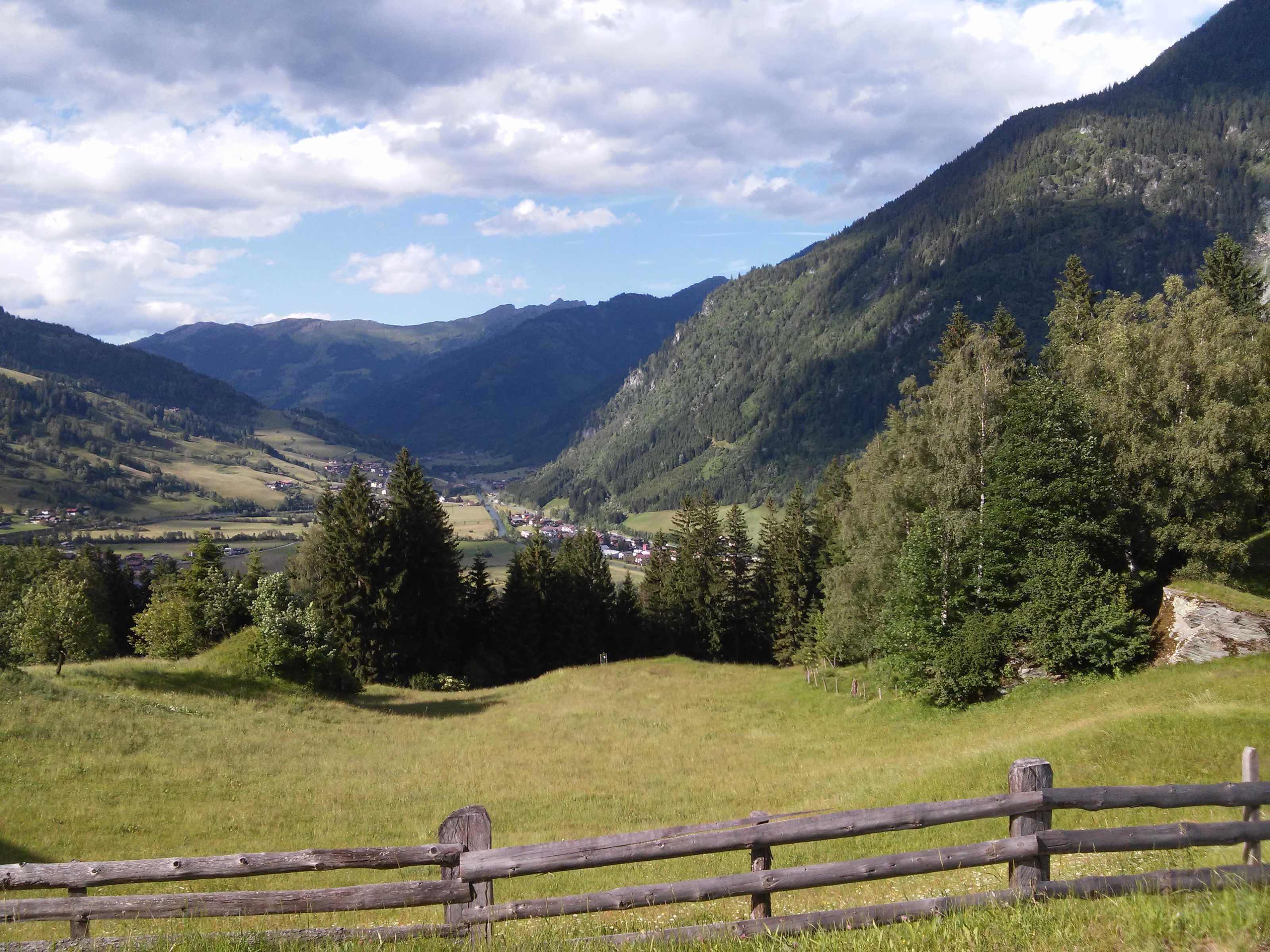 Un paysage rural avec une clôture en bois, des champs verdoyants et une vallée où se trouve un petit village.