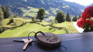 Une table en bois, sur laquelle se trouve un porte-clés en liège avec des clés, donnant sur un paysage montagneux avec des champs verdoyants et un village.