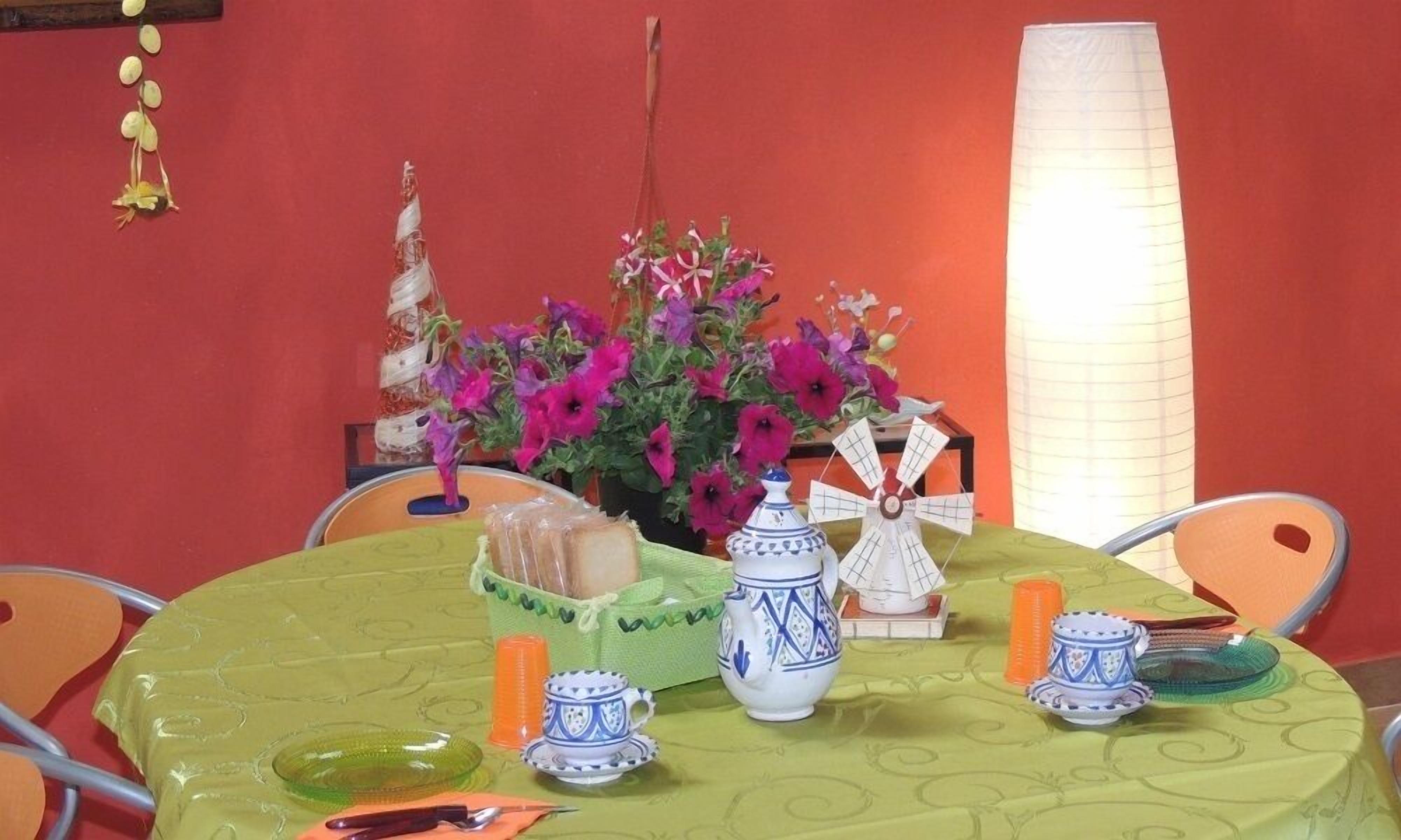 A table set with a green tablecloth, a vase with purple flowers, a decorative windmill, and various ceramic items.