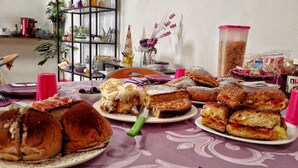 Een tafel met verschillende gebakjes en belegde broodjes, een koffieapparaat en een plank met keukengerei.