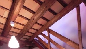 Een kleine kamer onder de dakpannen, met een schuine kap, een enkel bed, een stoel en een hangende lamp.