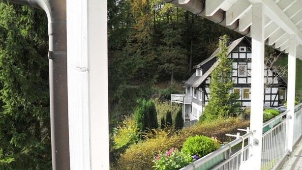 A balcony with a view of a traditional house surrounded by greenery. - Ferienwohnung van Balkom (Schmallenberg)