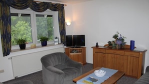 A living room with a grey armchair, a wooden coffee table, a television, and a cabinet with decorative items. - Ferienwohnung van Balkom (Schmallenberg)