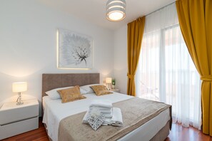 A neatly made bed with a white and beige bedspread, two pillows, and a folded towel on a wooden floor. - Tonina Apartments (Trogir)