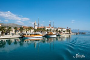 A harbor with boats docked, a building with a tower, and palm trees along the waterfront. - Tonina Apartments (Trogir)