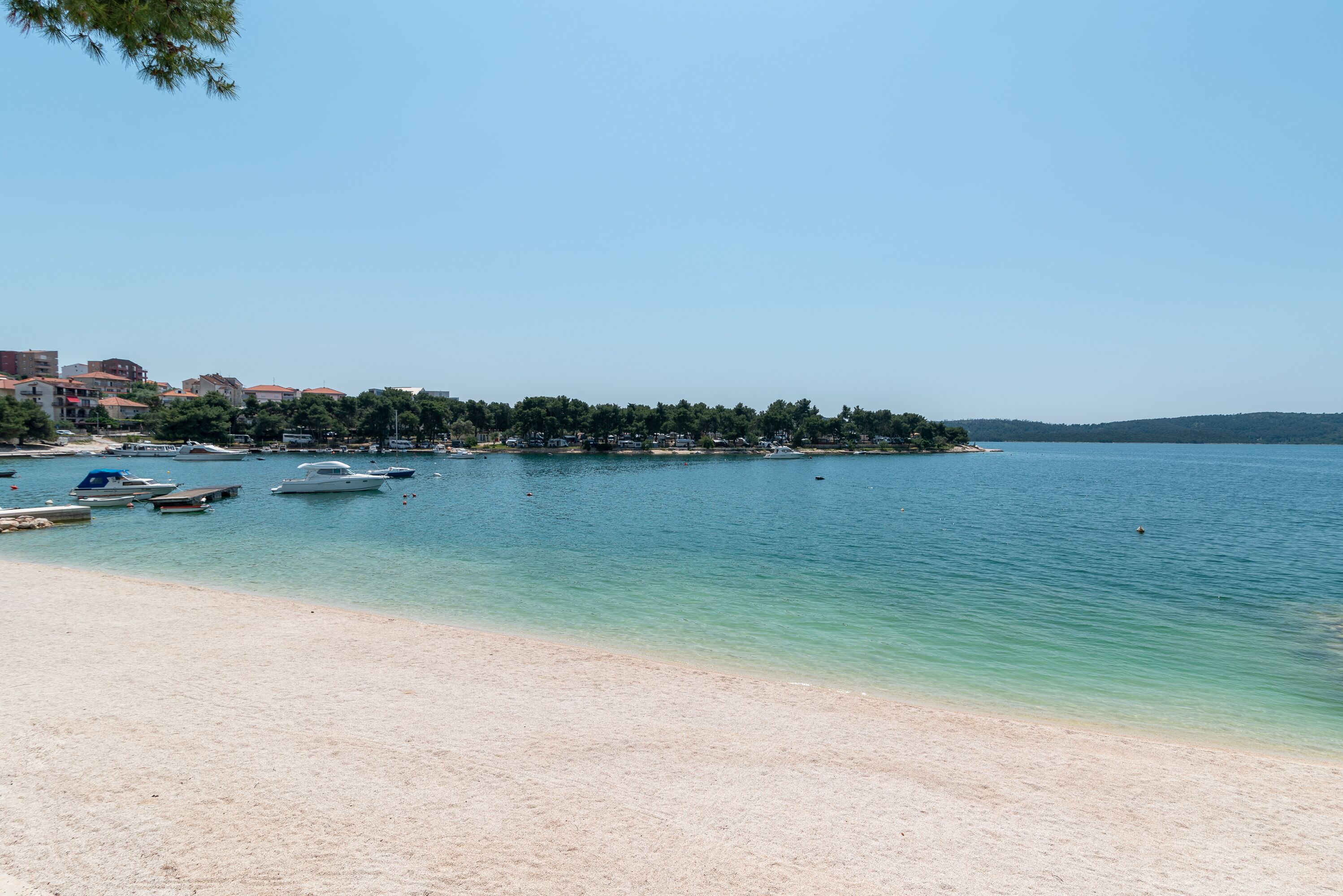 A beach with boats, a clear sky, and buildings in the background.