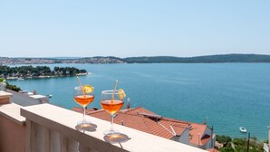 Two glasses of amber-colored beverage with lemon slices on a balcony overlooking a body of water with distant land and buildings.