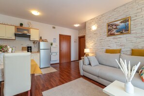 A modern kitchen with wooden cabinets, a built-in oven, and a dining area with a yellow tablecloth. - Tonina Apartments (Trogir)