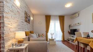 A modern living room with a stone wall, a sofa, a coffee table, a TV, and a dining area with a table and chairs.