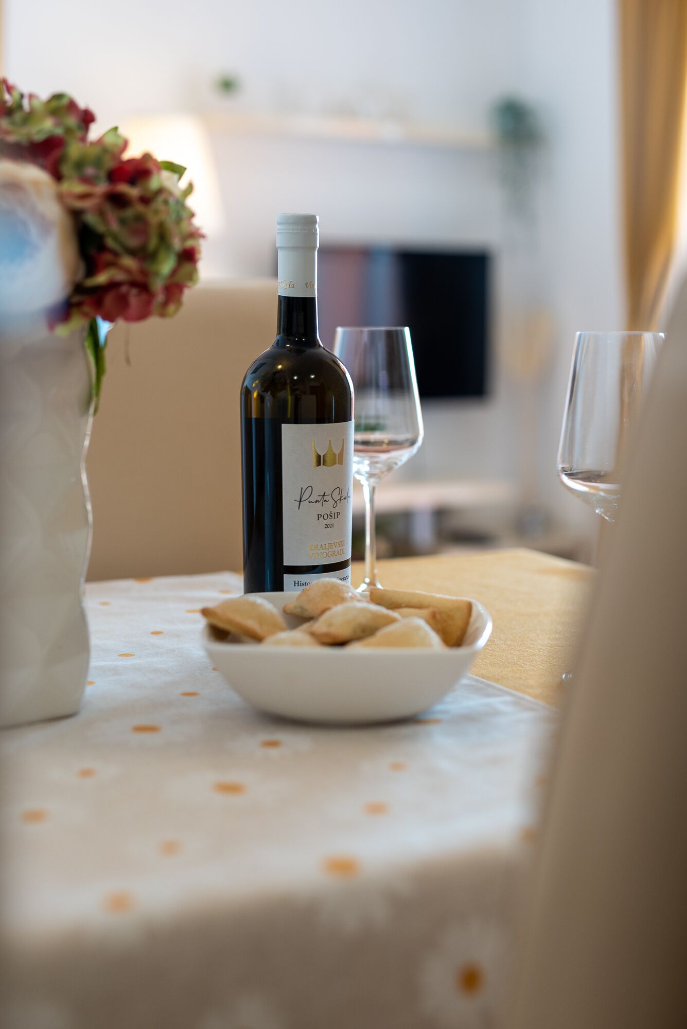 A dining table with a bottle of wine, two glasses, and a plate of pastries.
