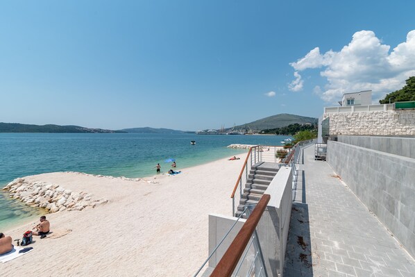 A coastal view with a beach, clear water, and a stone wall. - Tonina Apartments (Trogir)