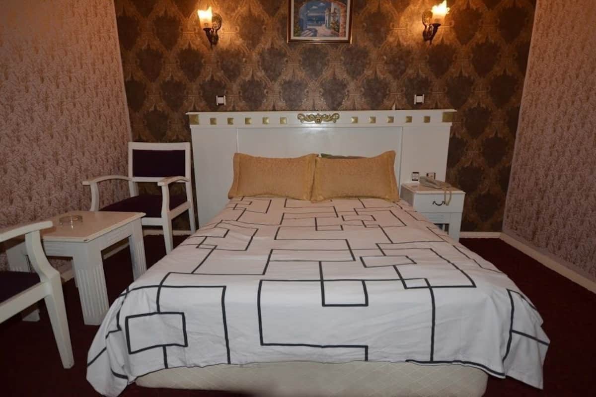 A hotel room with a bed, a chair, a nightstand, and two wall sconces.