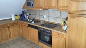 A kitchen with wooden cabinets, a microwave, a sink, and an oven. - Ferienwohnung Markus (Schmallenberg)