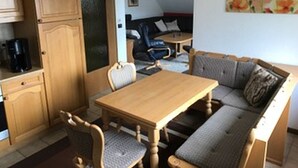 A compact living space with a wooden dining table, two chairs, a sofa, a coffee maker, and a small kitchen area with cabinets. - Ferienwohnung Markus (Schmallenberg)