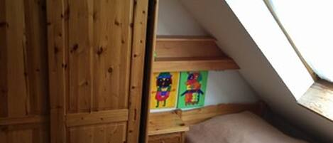 A bedroom with a wooden wardrobe, a bed, a desk with colorful artwork, and a skylight.