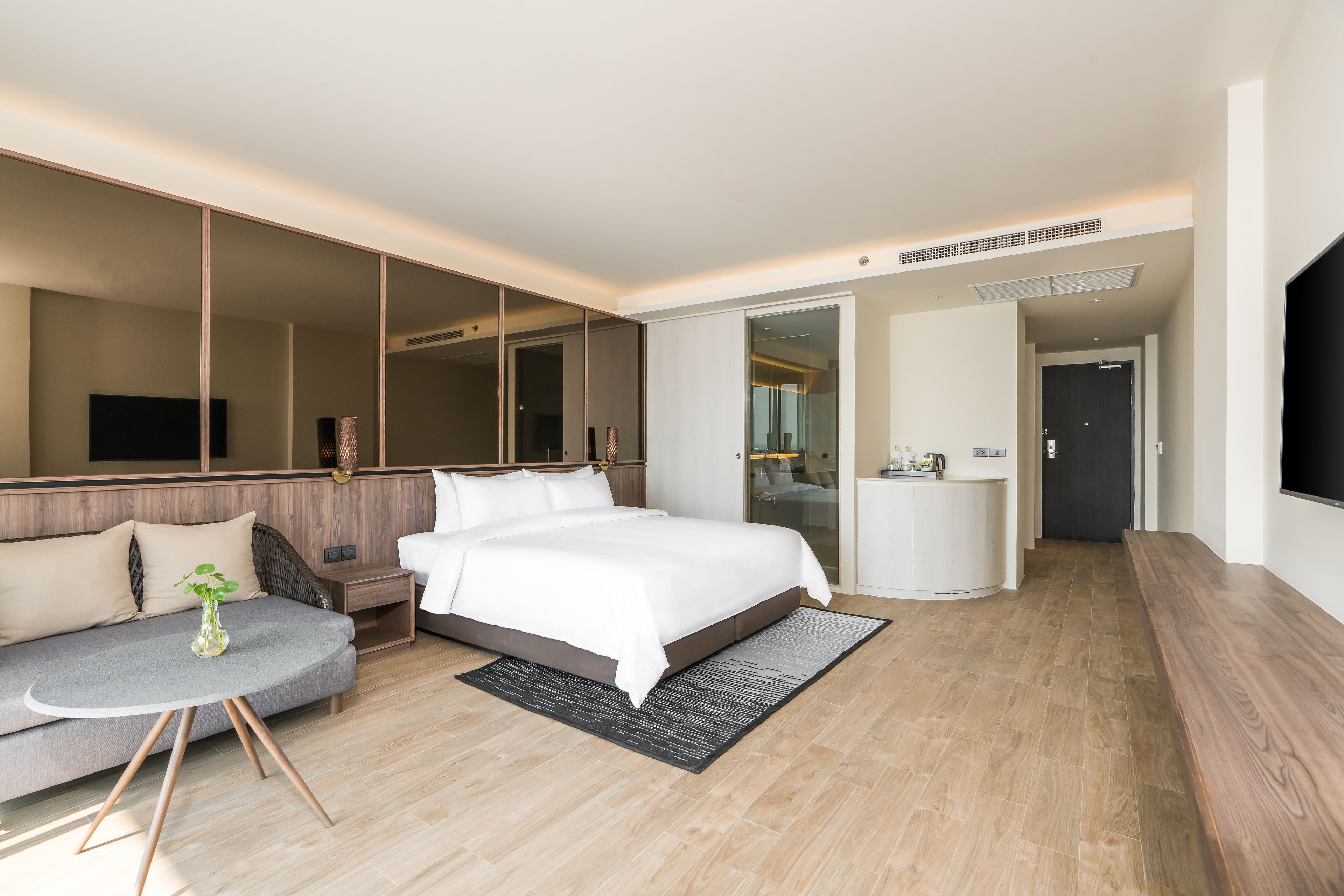 Een moderne hotelkamer met een groot bed, een bank, een kleine tafel met een plant, een grote spiegel en een televisie.
