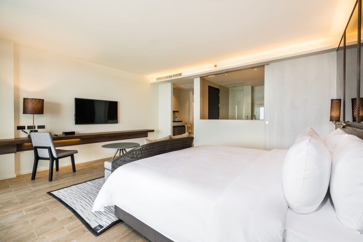 Ett modernt hotellrum med en stor säng, ett skrivbord med en stol, en platt-TV och en liten matplats.