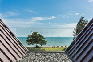 Un bâtiment moderne doté d’un toit en pente et offrant une vue dégagée sur la mer, un arbre et un espace verdoyant aménagé avec des chaises longues.
