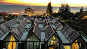 Un complexe hôtelier comprenant plusieurs bâtiments, une piscine et offrant une vue sur l’océan au coucher du soleil.