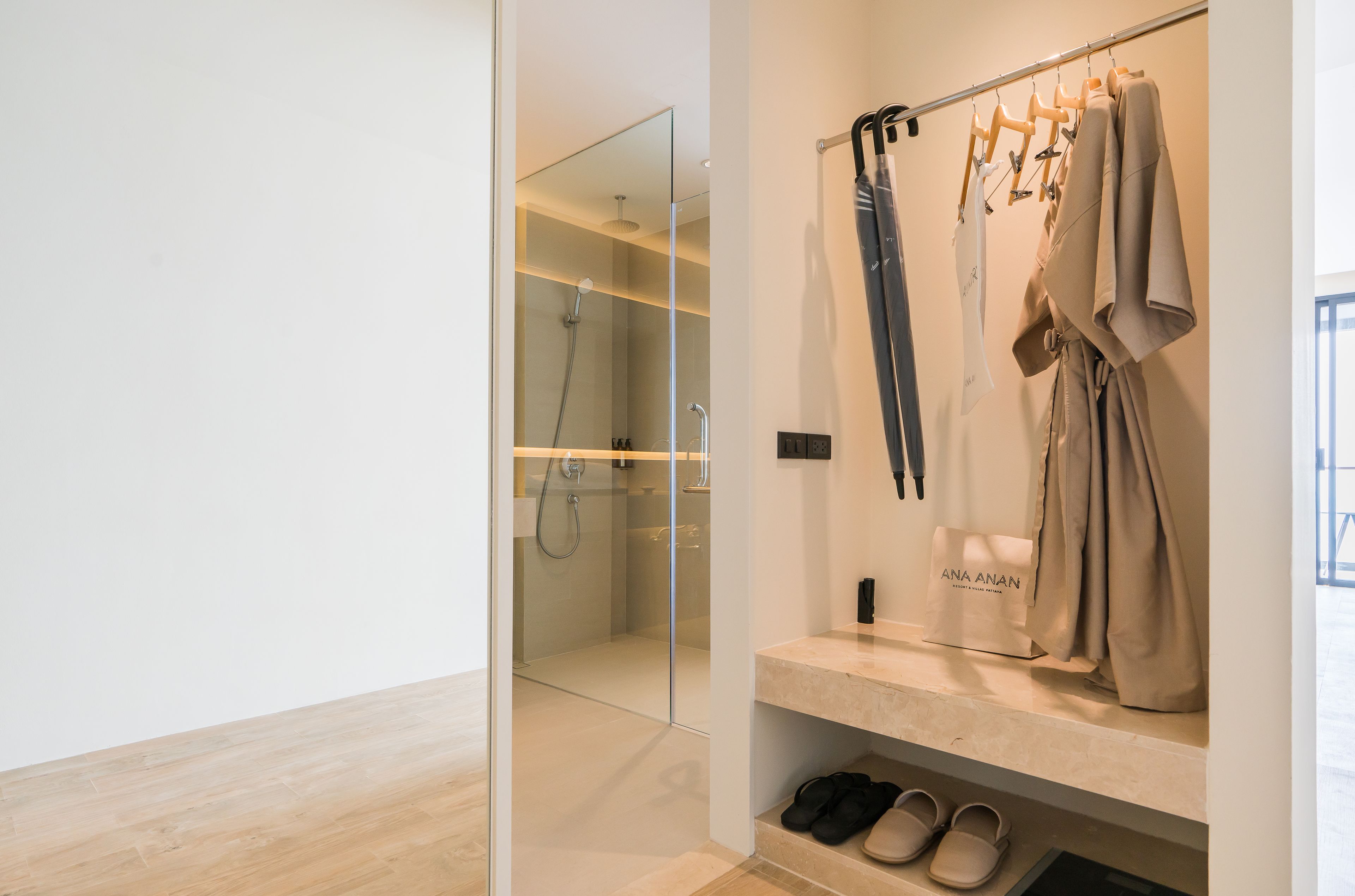 A modern bathroom with a glass-enclosed shower, a vanity with a beige countertop, and a clothing rack with hanging garments.
