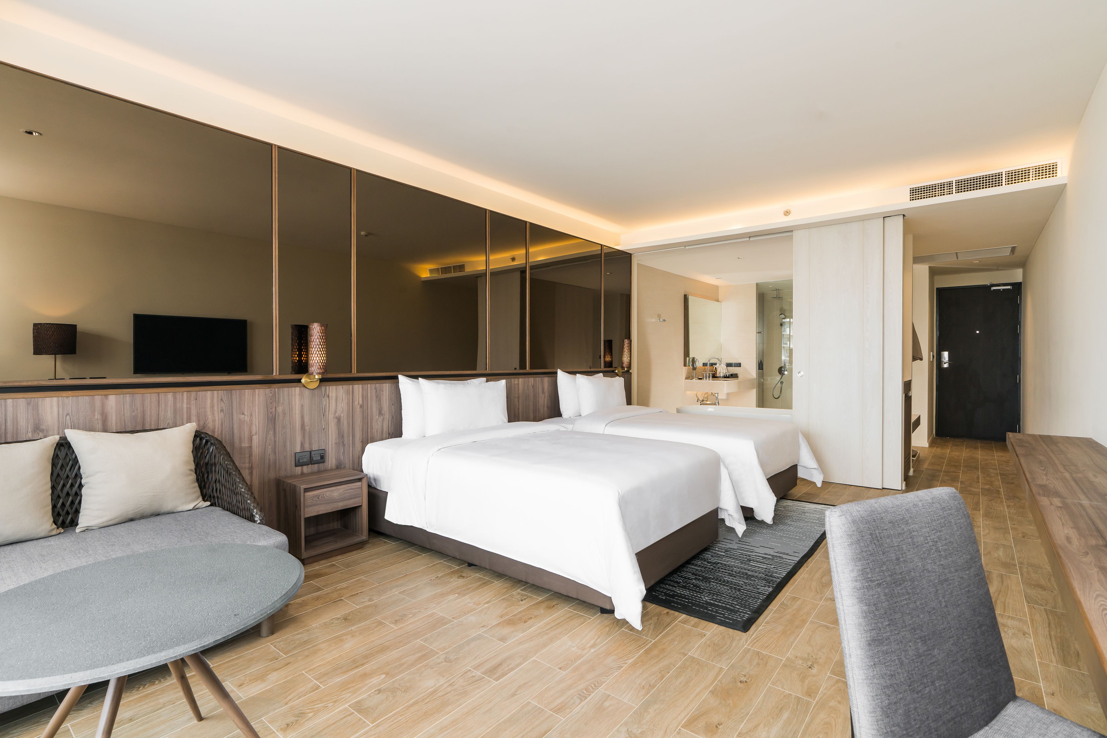 A modern hotel room with two beds, a seating area, and a large mirror.