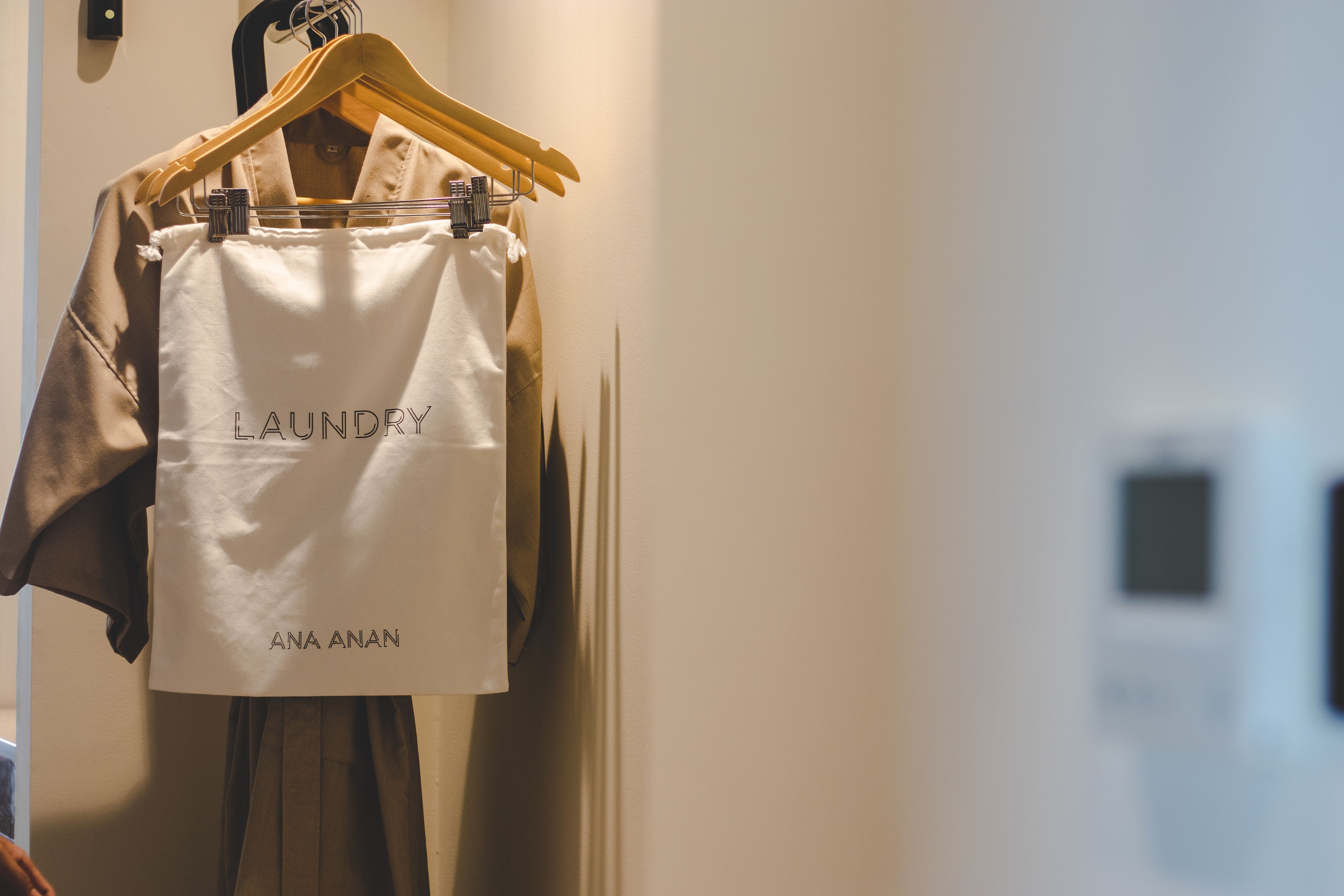 A white laundry bag hanging on a wooden hanger with the text "LAUNDRY ANA ANAN" visible.