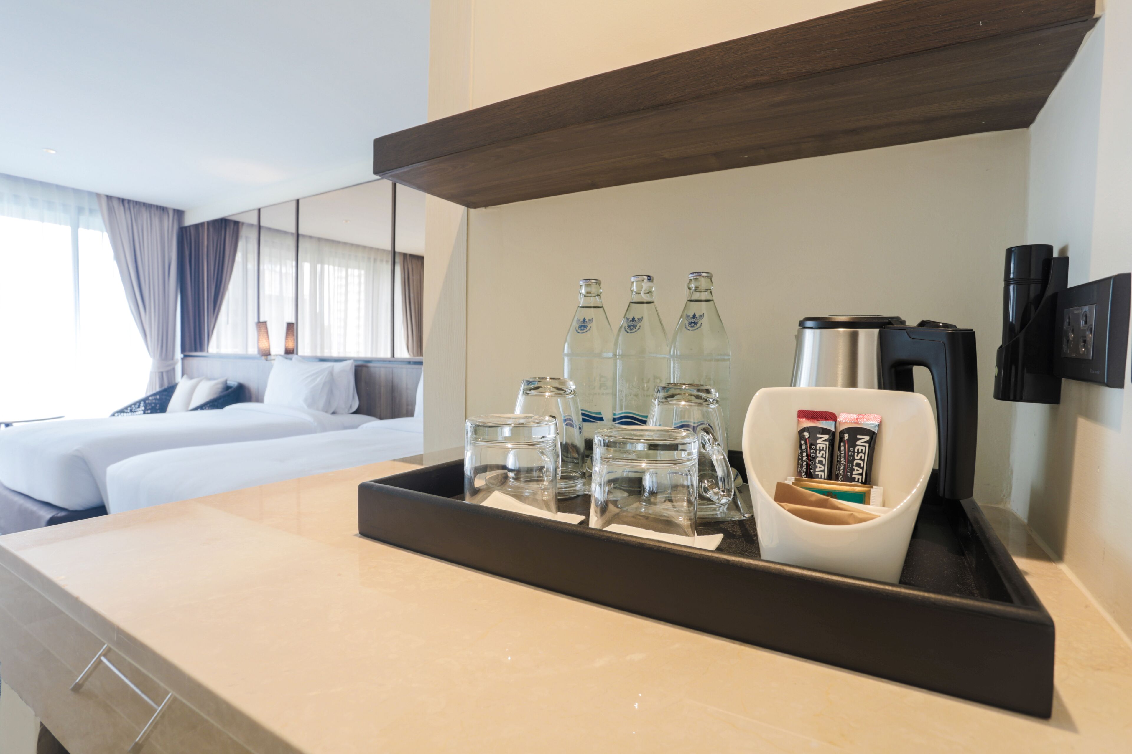 A hotel room with a bed, a tray with bottles and a coffee maker, and a mirror on the wall.