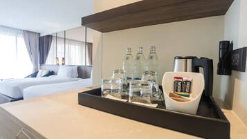 A hotel room with a bed, a tray with bottles and a coffee maker, and a mirror on the wall.