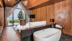 Une salle de bain moderne avec une baignoire sur pieds, un lambris en bois et une grande fenêtre donnant sur l’extérieur.