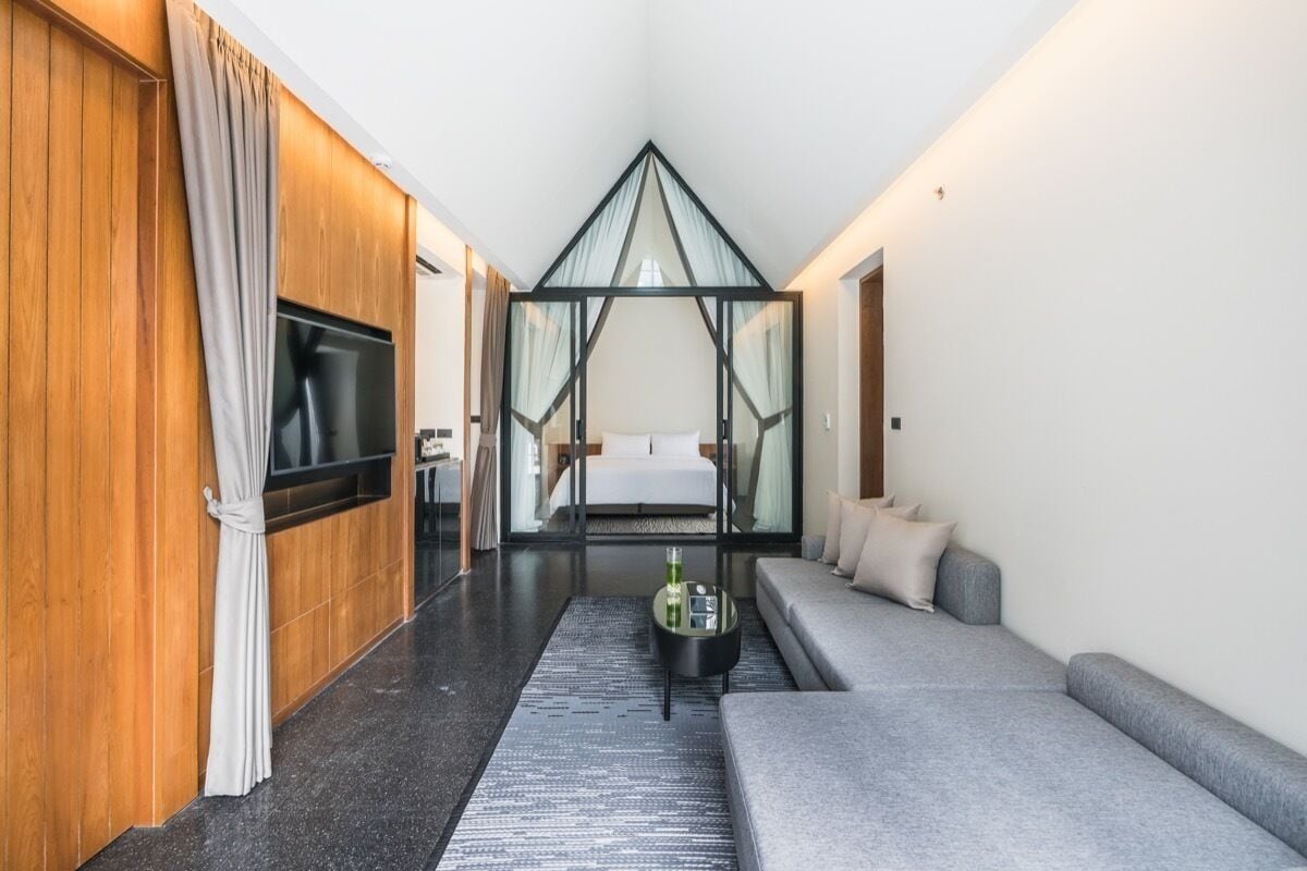 A modern hotel room with a large bed, a sofa, a TV, and a glass partition.
