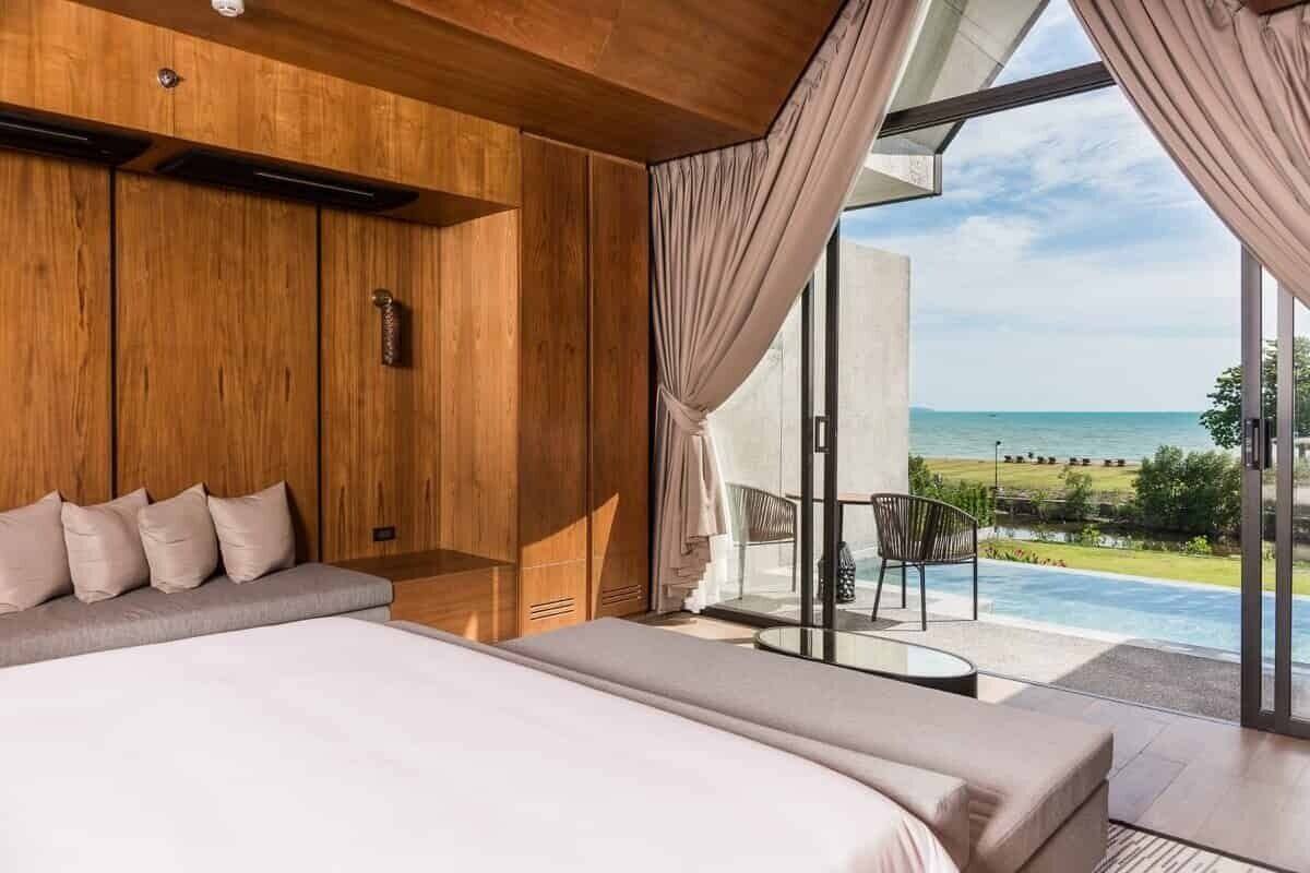 Une chambre moderne avec un grand lit, un lambris en bois et une vue sur une piscine et une plage.