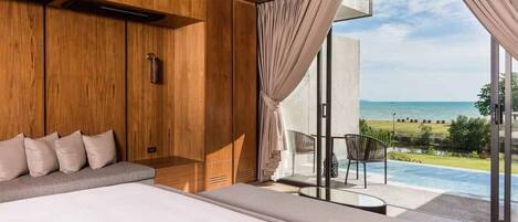 A modern bedroom with a large bed, wooden paneling, and a view of a pool and beach.