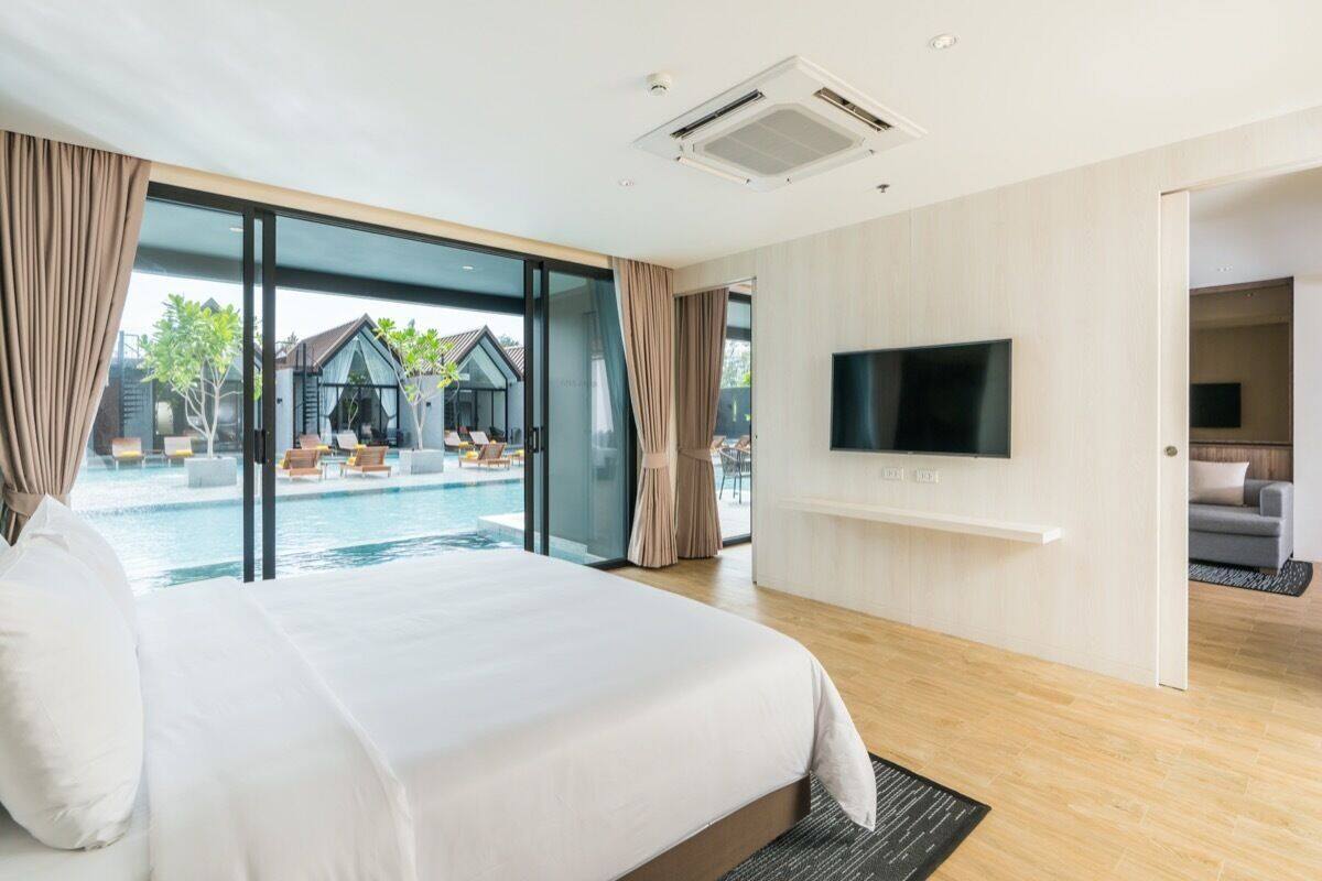 Une chambre d’hôtel moderne dotée d’un grand lit, d’un téléviseur fixé au mur et offrant une vue sur une piscine extérieure et une villa.
